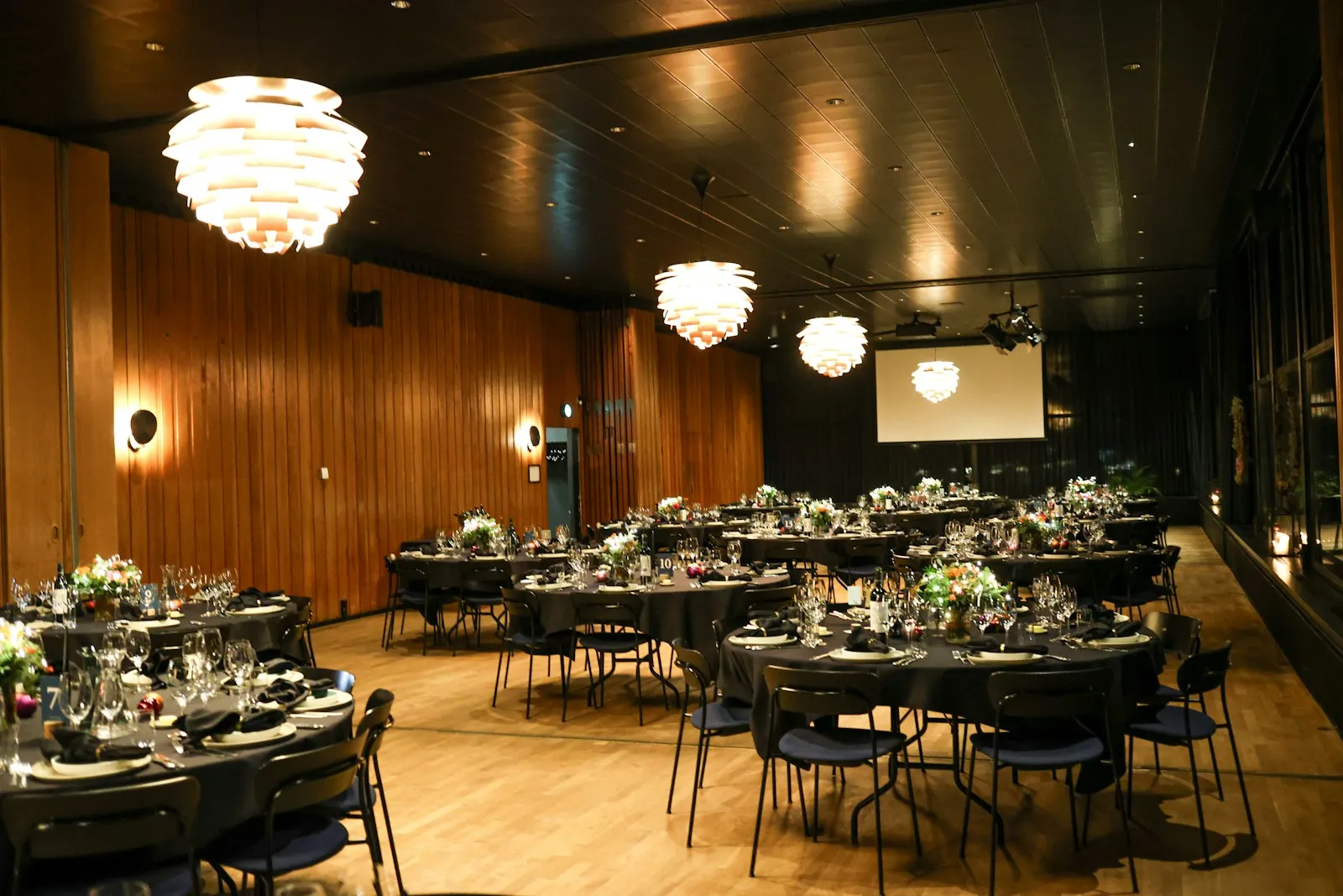 Event hall laid with round dining tables, pendant lamps and a wood-panelled wall