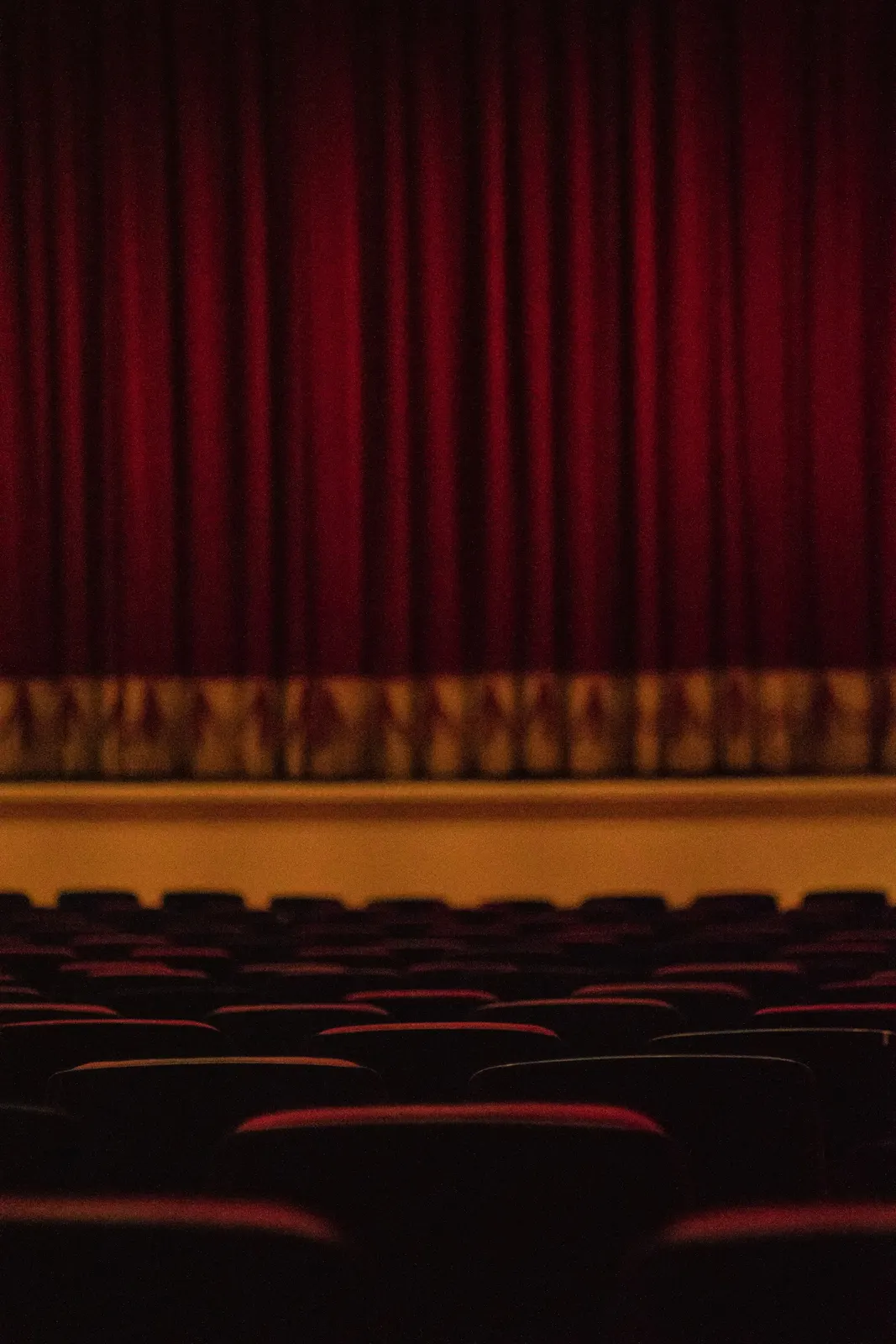 Rows of empty theatre seats facing a closed red stage curtain